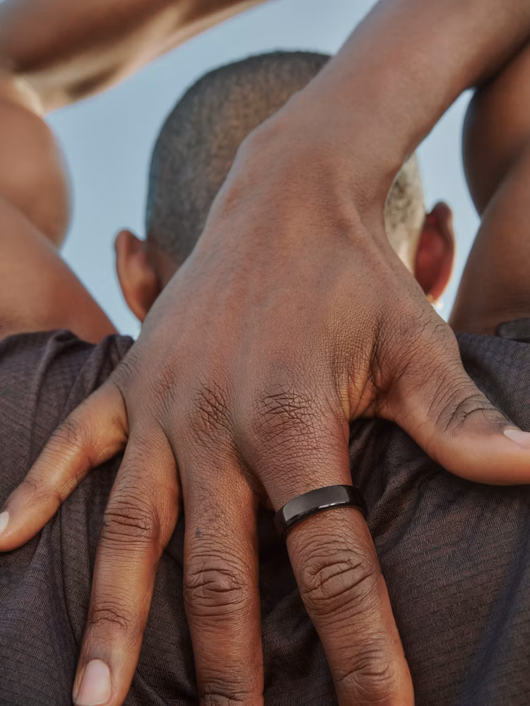 Close up of a person stretching his hands behind his head while wearing an Oura Ring 5 in black finish.