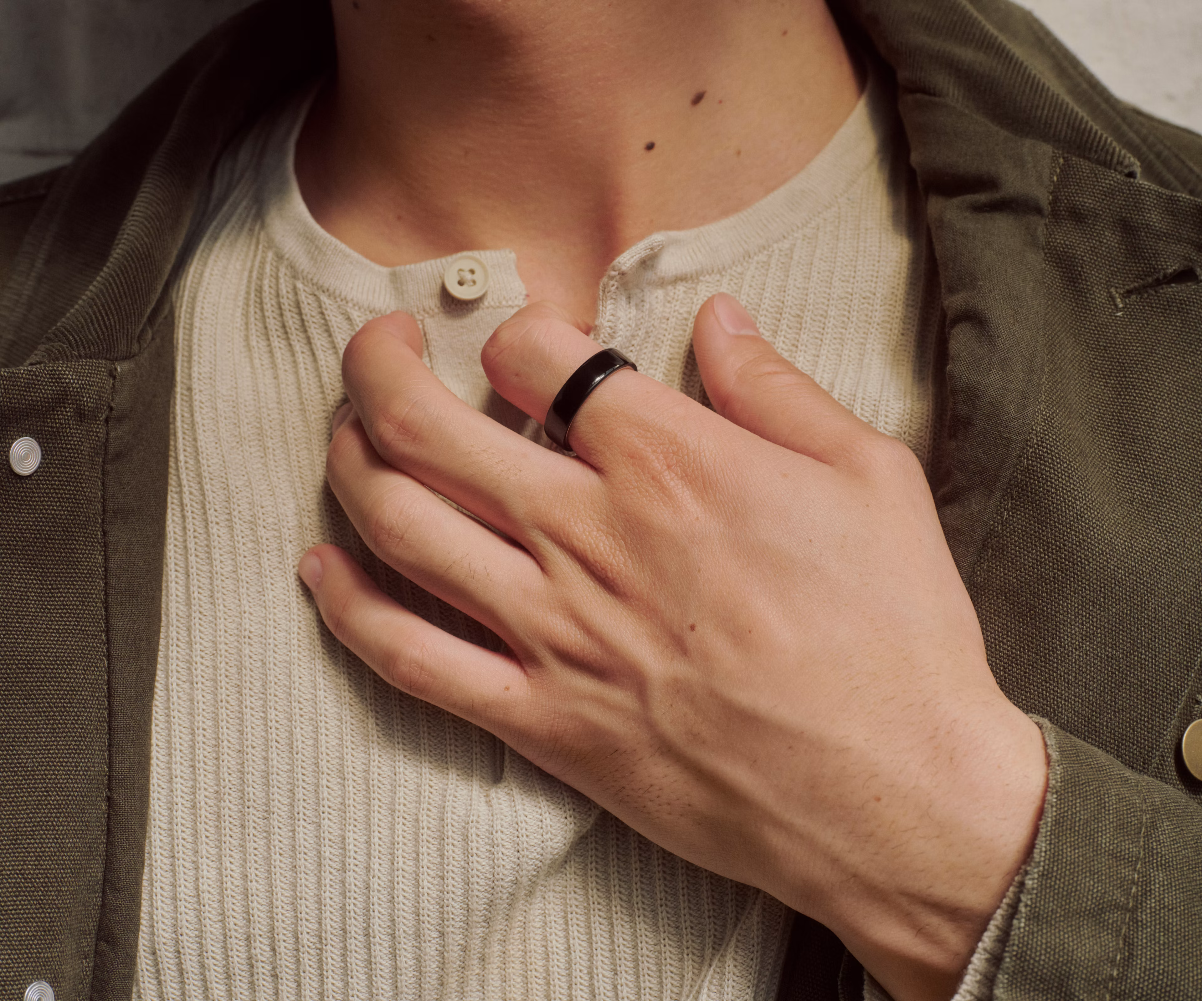 Close up of a person's hand resting against their chest with a Black Oura Ring 5 on their finger