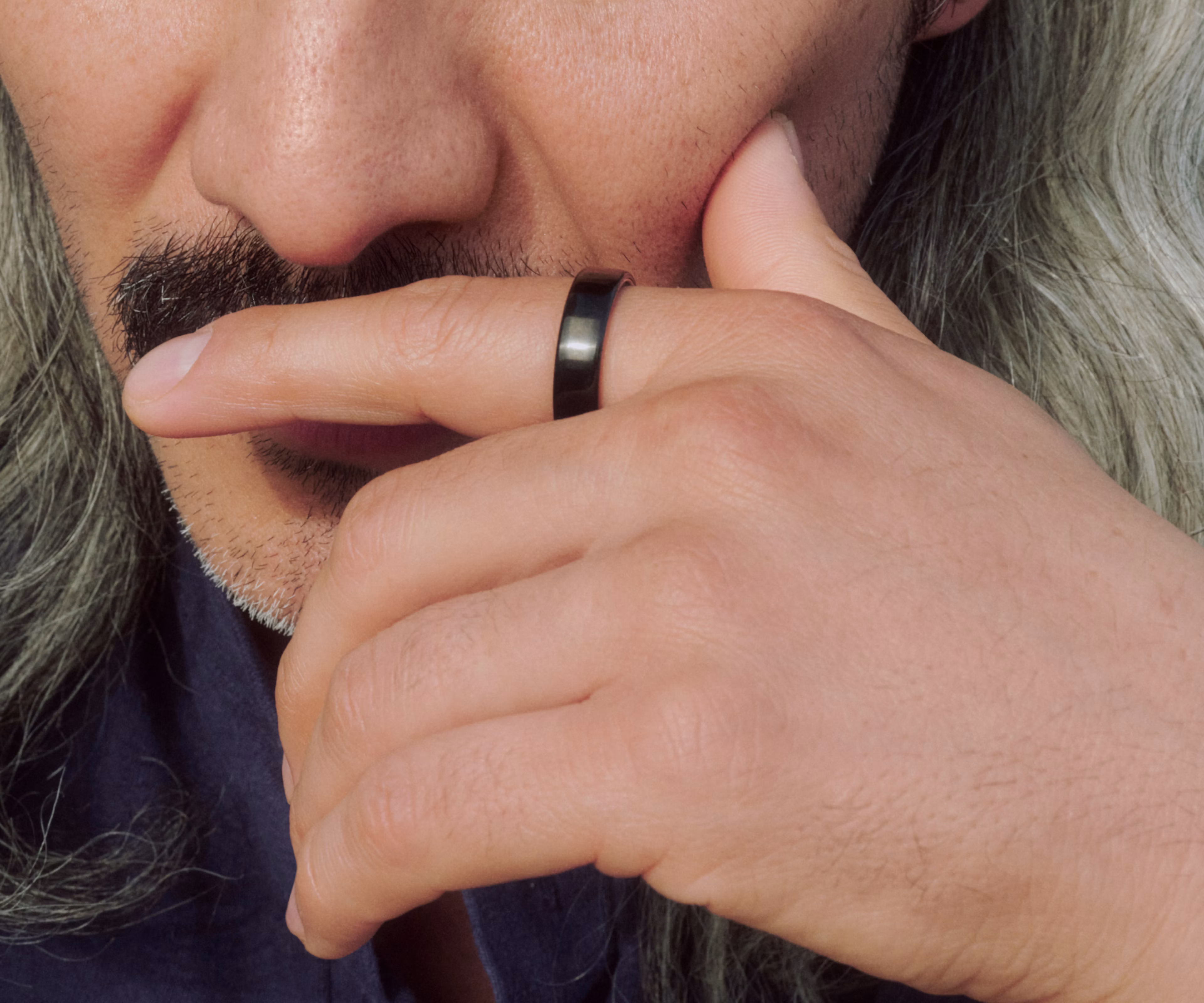Close up of a man holding his finger across his lips in a thoughtful pose while wearing a Black Oura Ring 5.