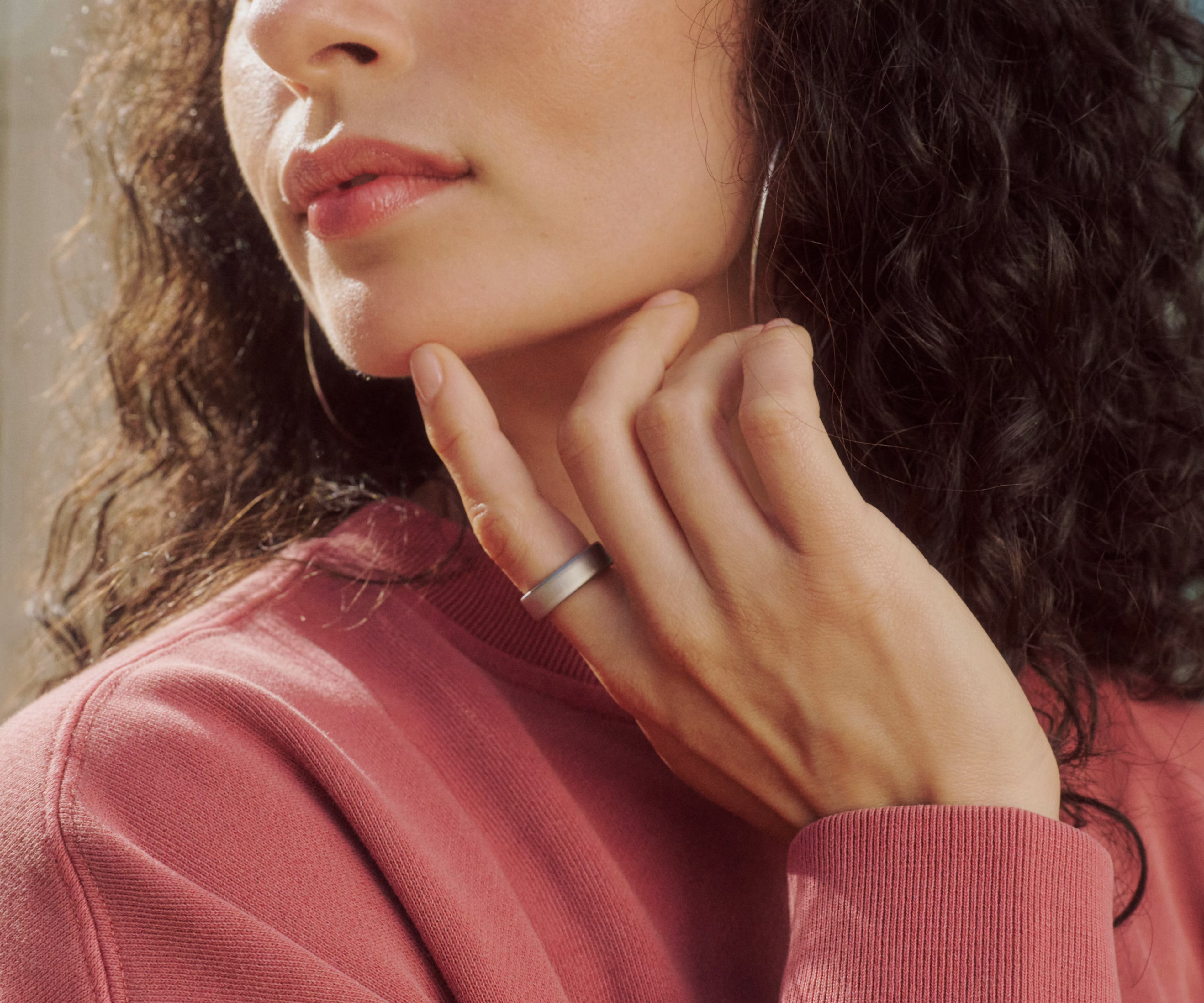 Close up of a person touching their chin, wearing a Brushed Silver Oura Ring 5 on their finger and a pink sweatshirt.