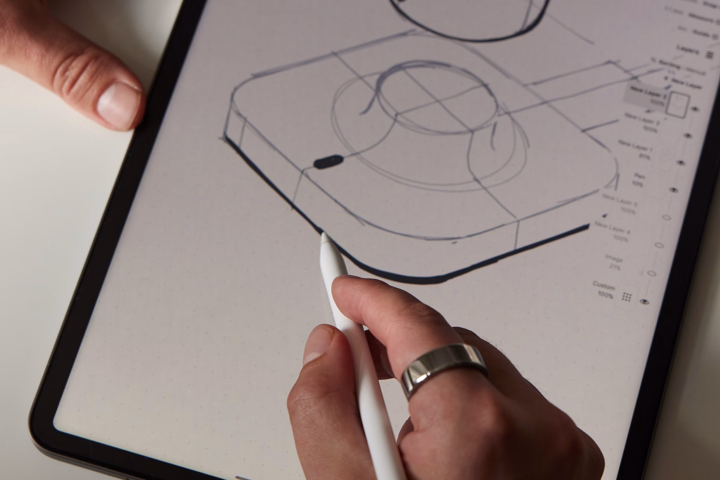A hand holding a tablet pencil wearing an Oura Ring drawing a picture of an Oura Ring charger