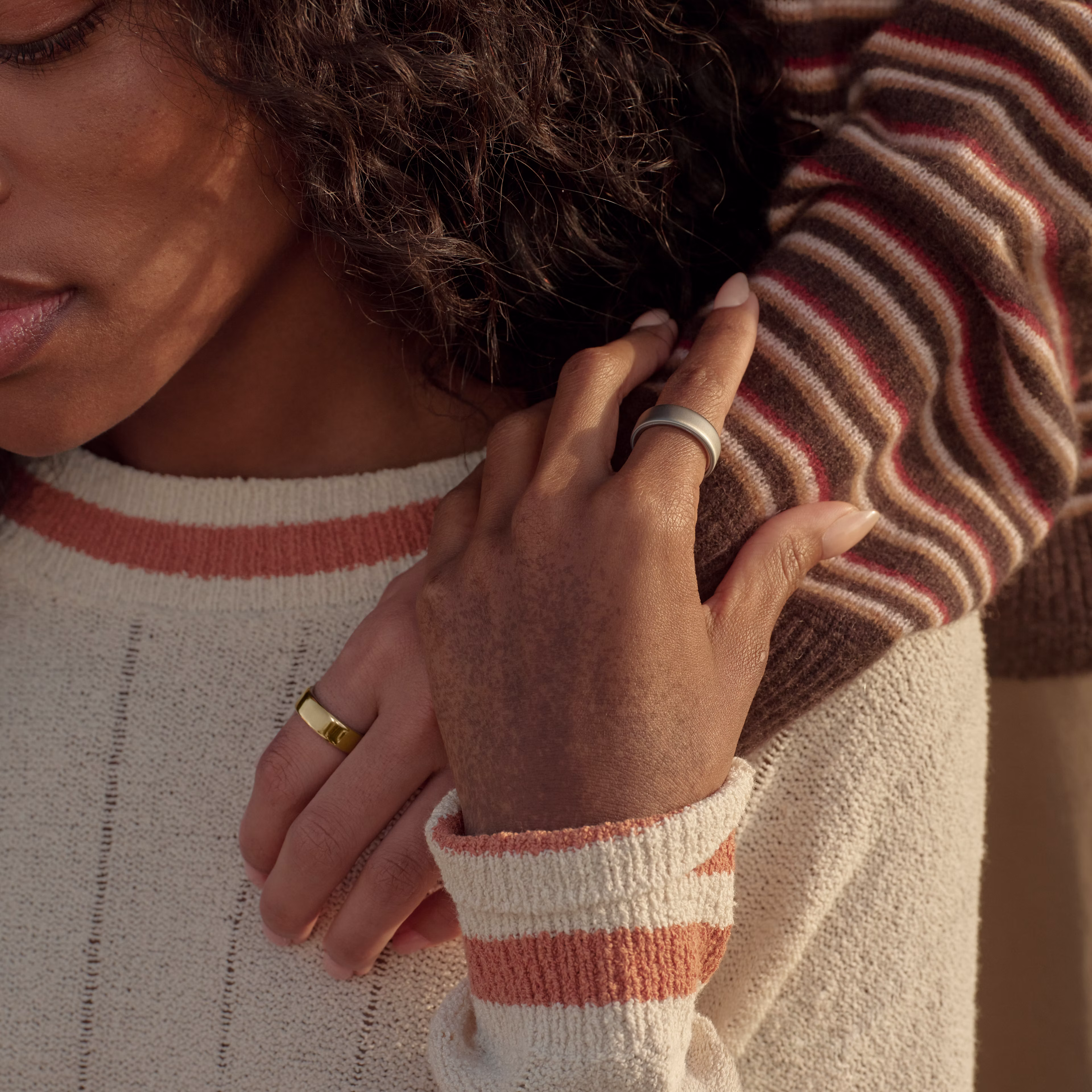 Close up of a person wearing an Oura Ring 5, with another person’s hand on their shoulder, also wearing an Oura Ring 5.