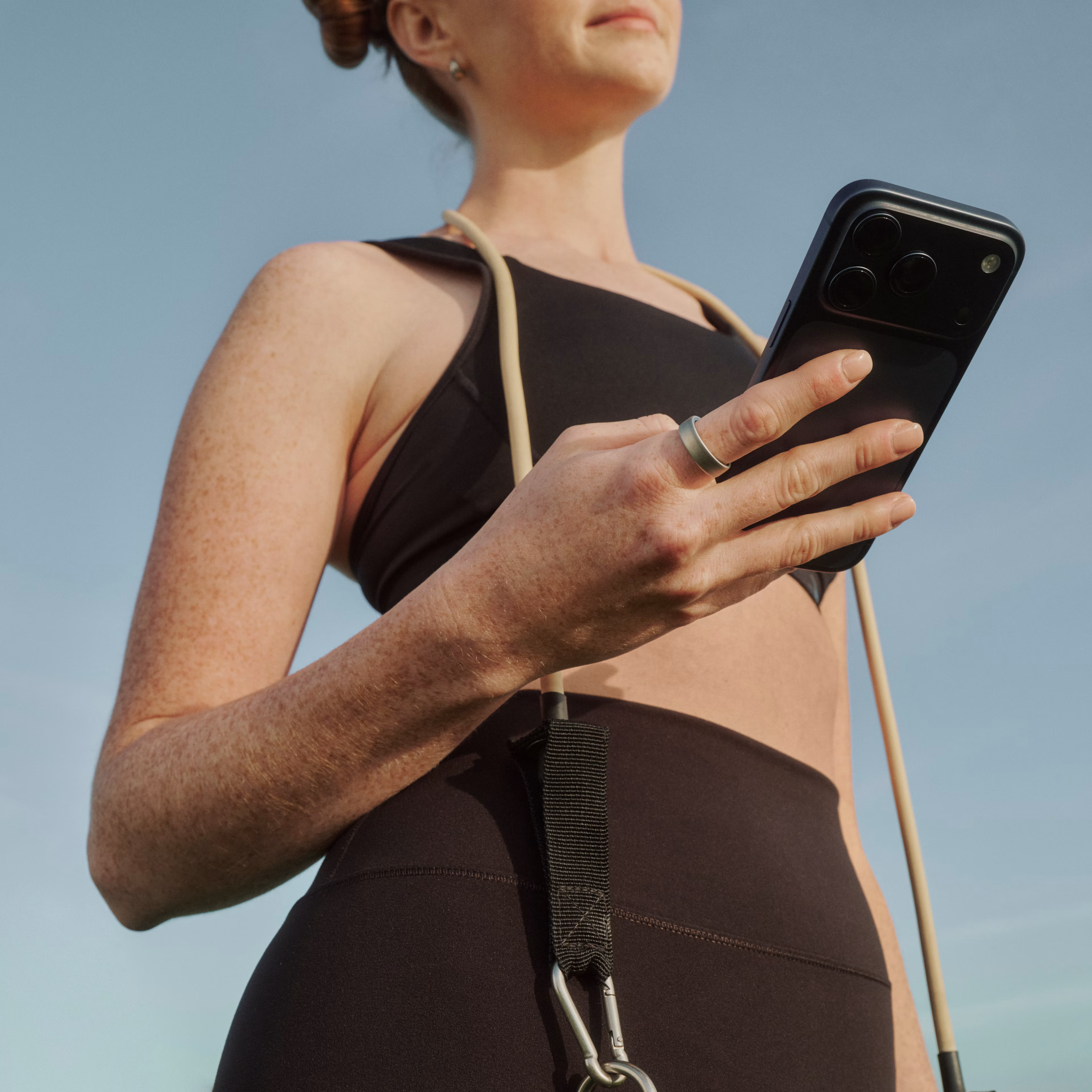 Person outdoors holding a smartphone while wearing an Oura Ring 5