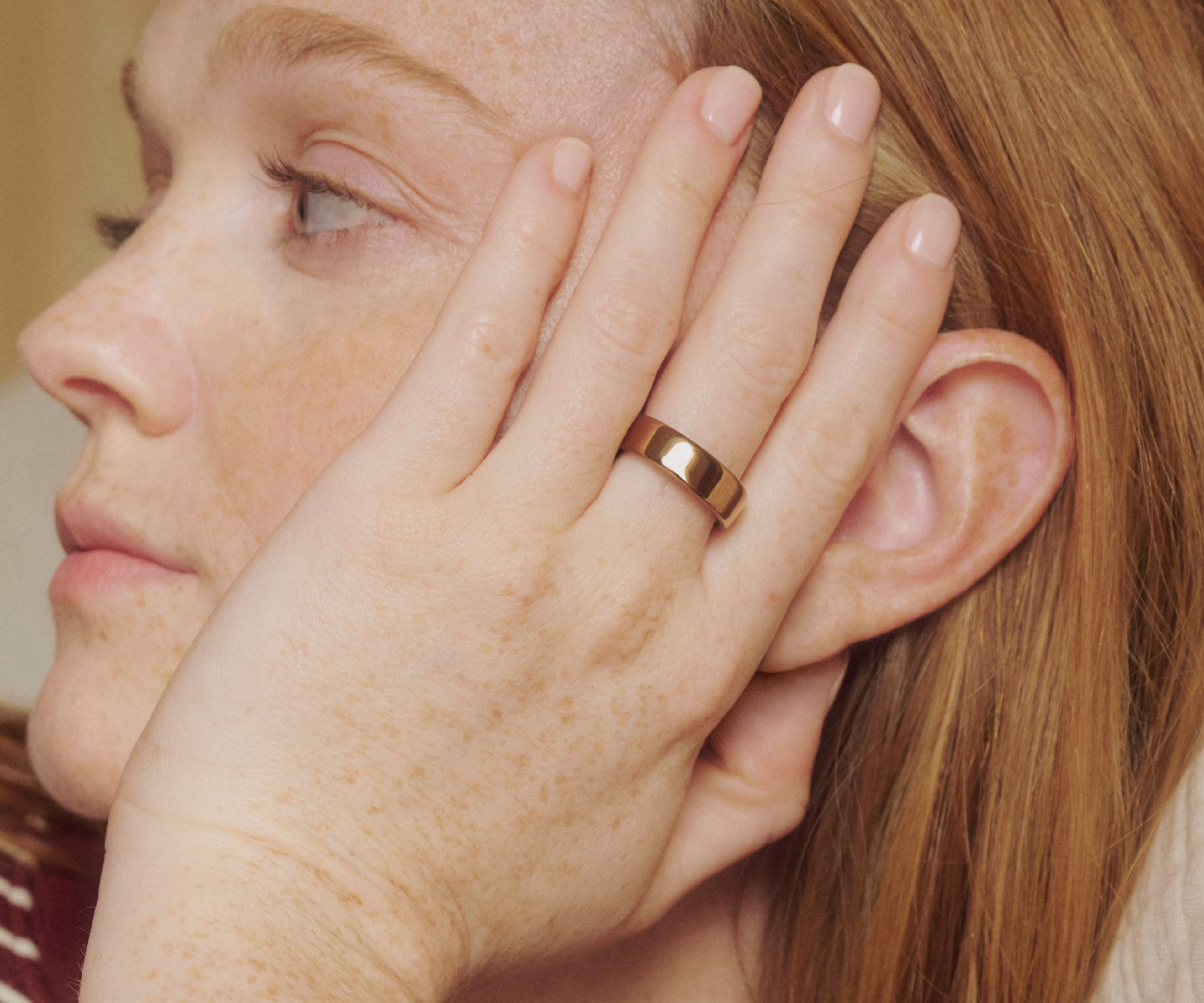 Close up of a person resting their hand on their face while wearing a Deep Rose Oura Ring 5.