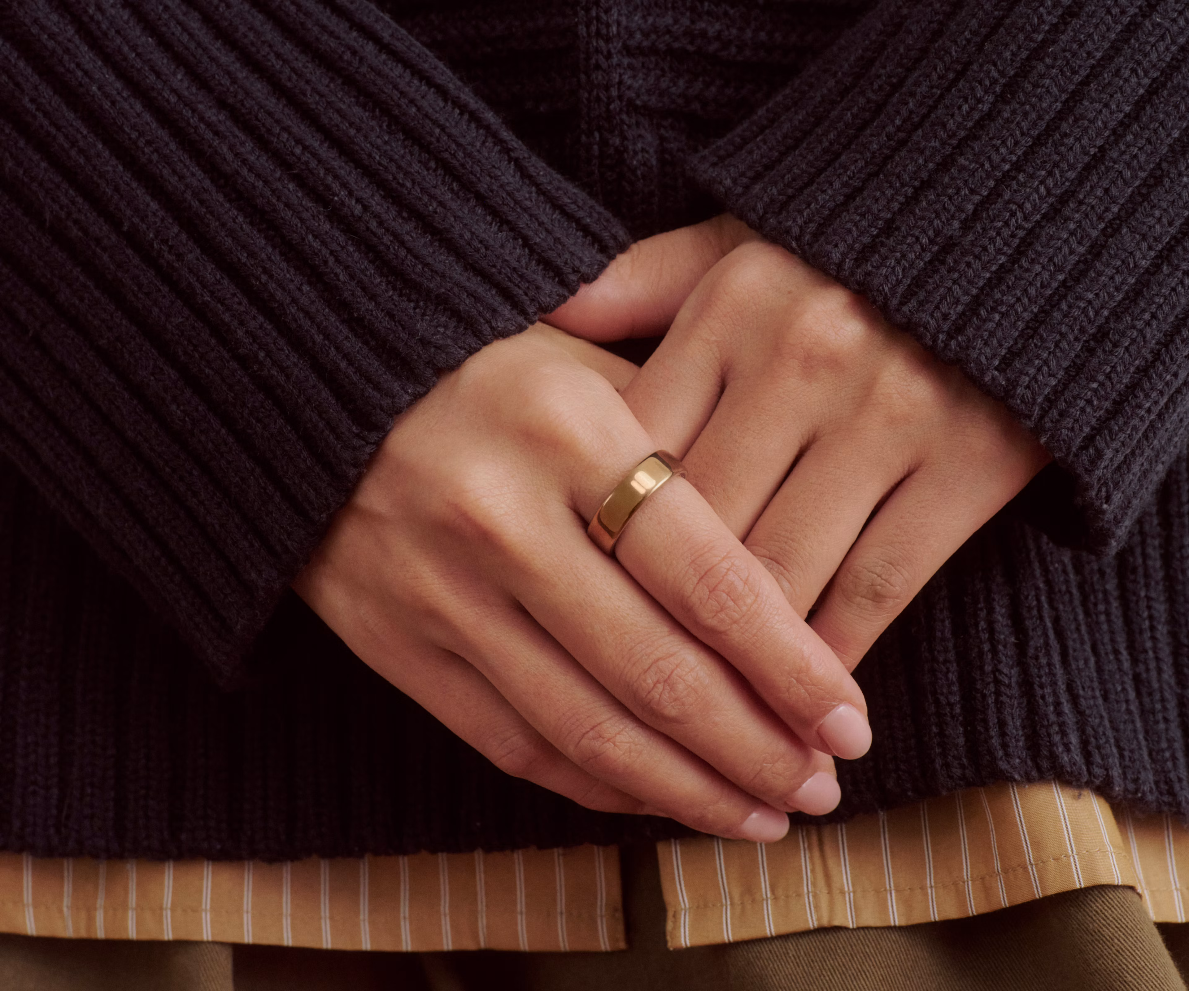 Close up of a person's hands resting in front of them with a Deep Rose Oura Ring 5 on their finger