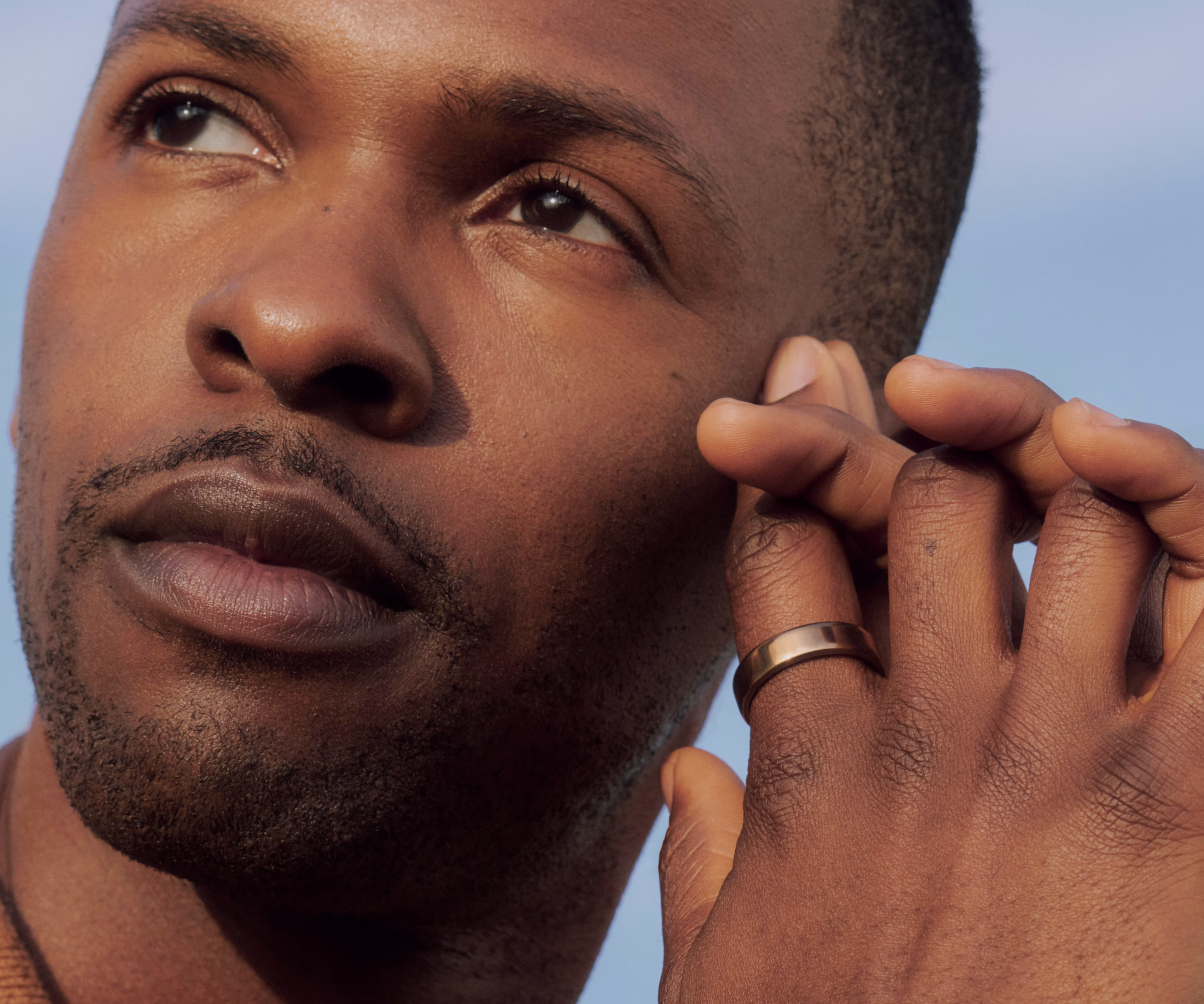 Close up of a man gazing upward, resting his hand near his face, wearing a Deep Rose Oura Ring 5 on his finger.