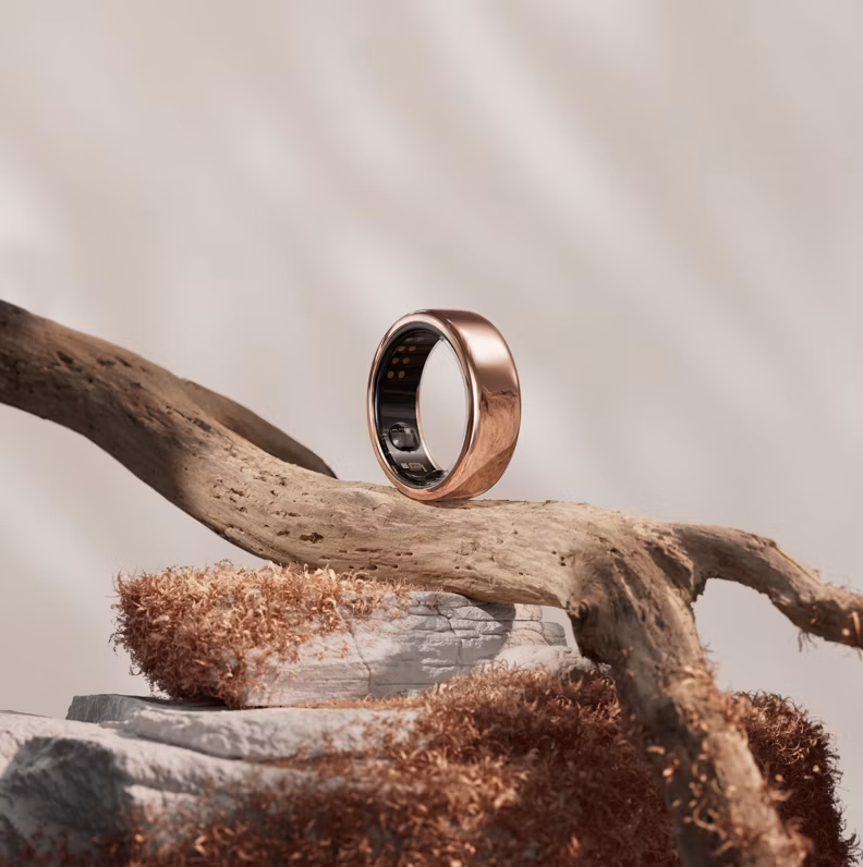 An Oura Ring in the Rose Gold finish balanced on a branch of driftwood