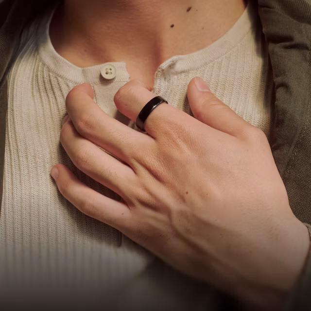 Close up of a person's hand resting against their chest with a Black Oura Ring 5 on their finger
