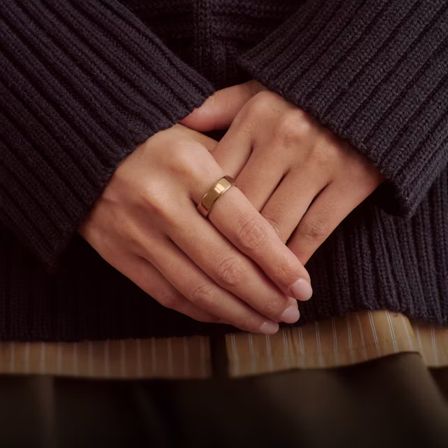 Close up of a person's hands resting in front of them with a Deep Rose Oura Ring 5 on their finger