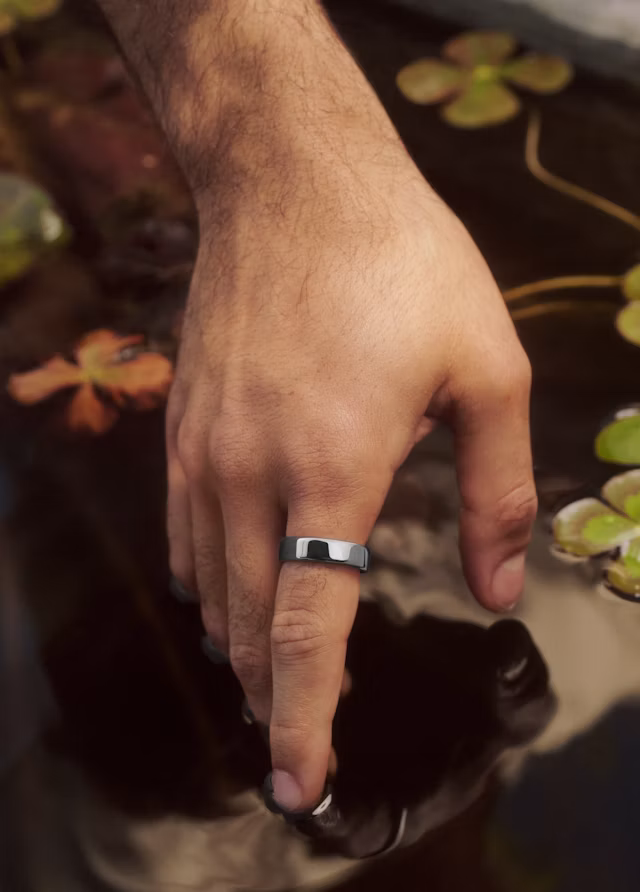 Close up of a hand wearing an Oura Ring 5 in Silver finish touching the surface of a pond