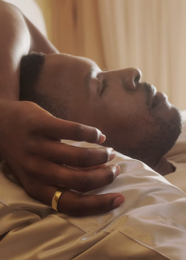 A man resting in bed wearing an Oura Ring 5 in Gold finish