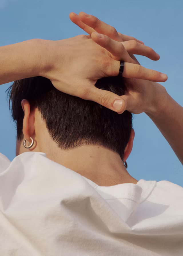 Close up of the back of a person's head with their hands interlocked behind it while wearing an Oura Ring 5 in Black finish