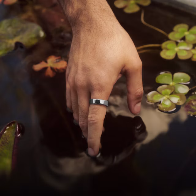 Close up of a person's hand touching the surface of a decorative pond with a Silver Oura Ring 5 on their finger