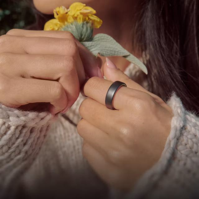 Close up of a person's hands holding a flower with a Stealth Oura Ring 5 on their finger