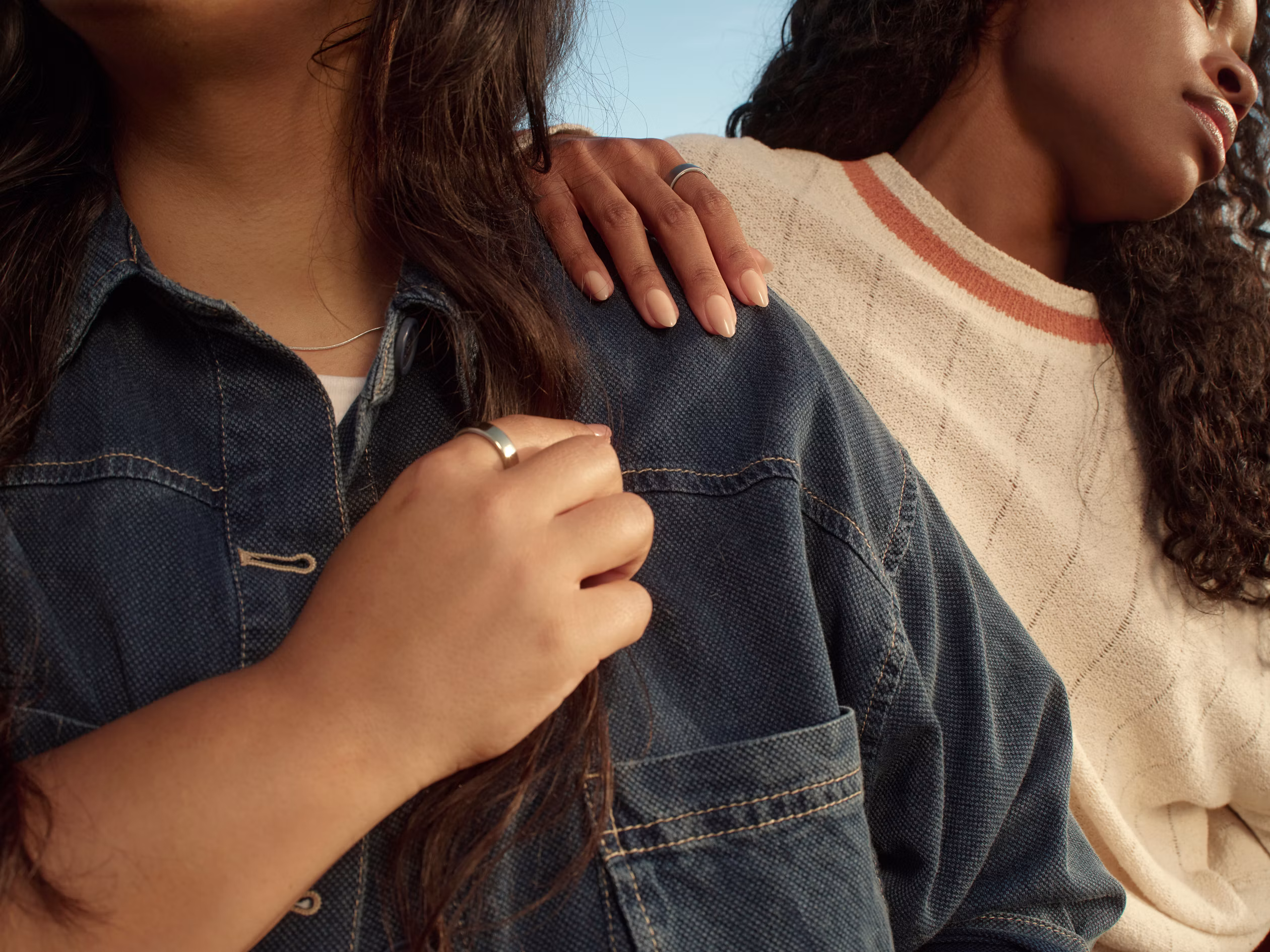 Two people wearing Silver Oura Rings, with one resting a hand on the other's denim-clad shoulder.