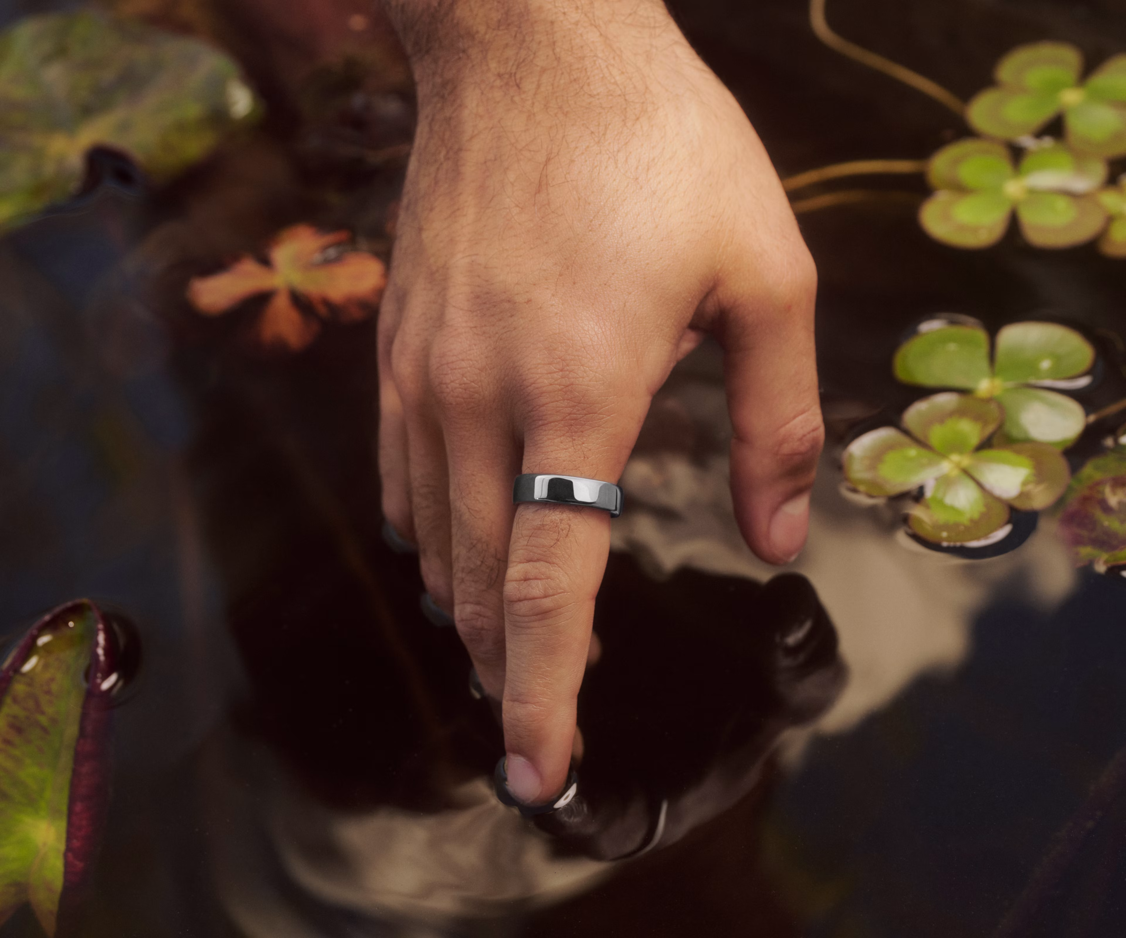 Close up of a person's hand touching the surface of a decorative pond with a Silver Oura Ring 5 on their finger