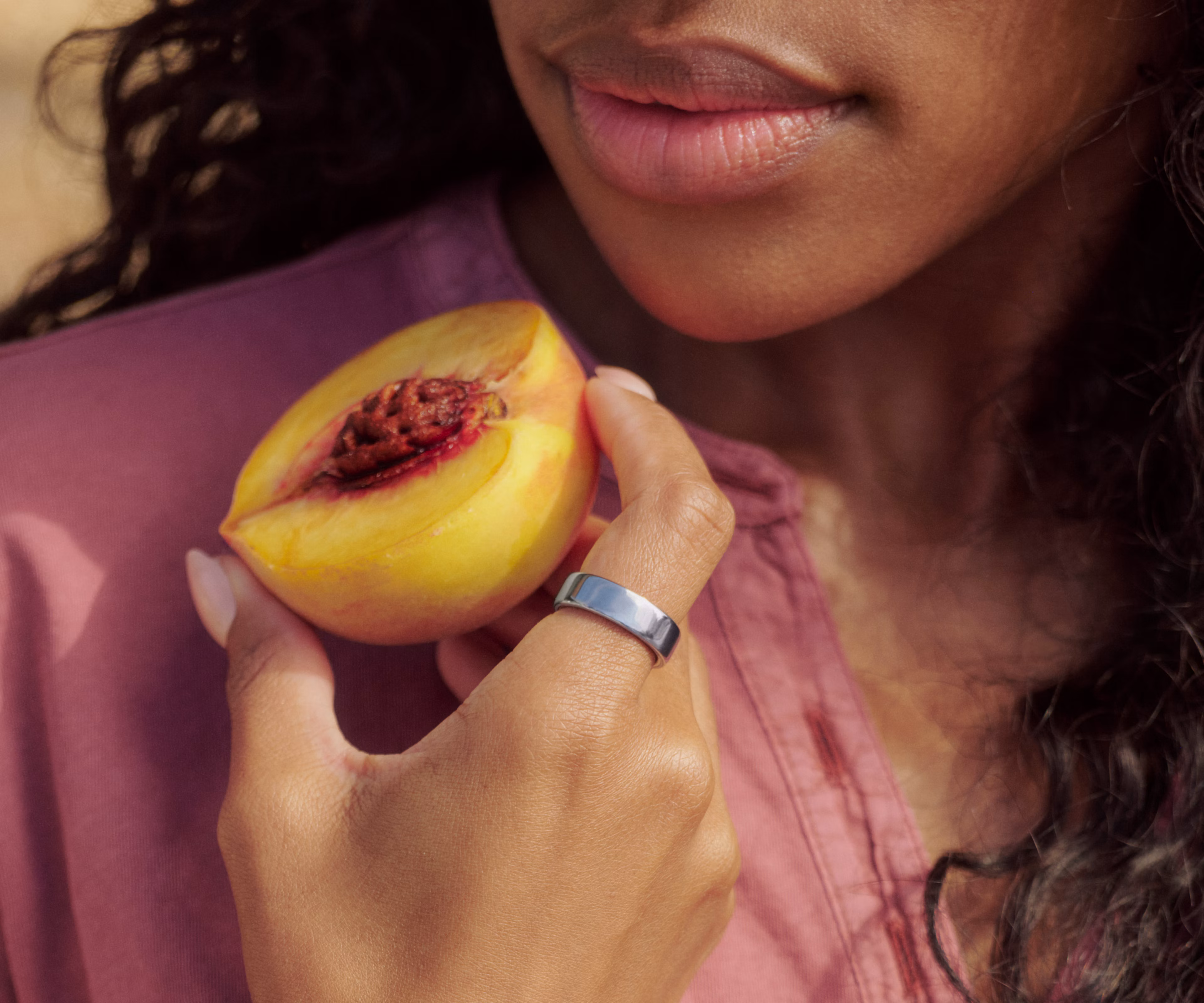 A close up of a person holding a fruit while wearing a Silver Oura Ring 5 on their finger.