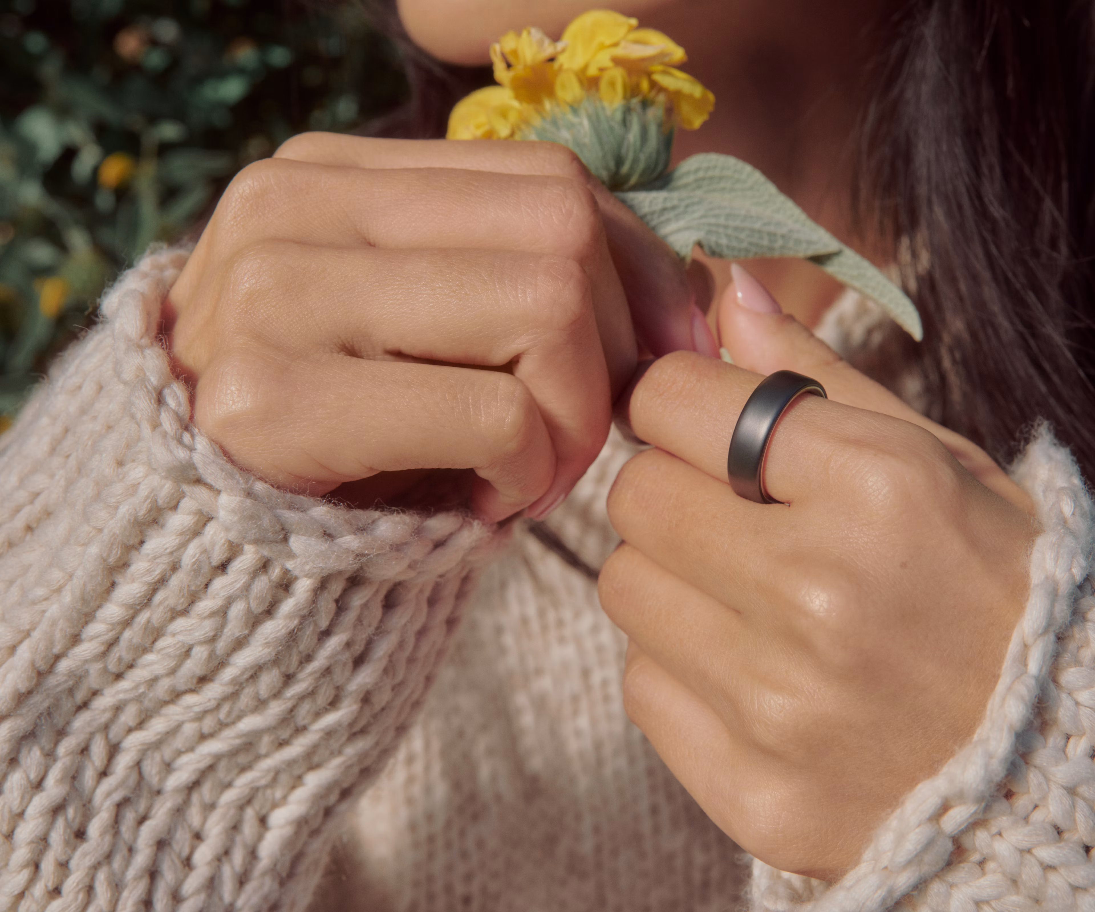 Close up of a person's hands holding a flower with a Stealth Oura Ring 5 on their finger