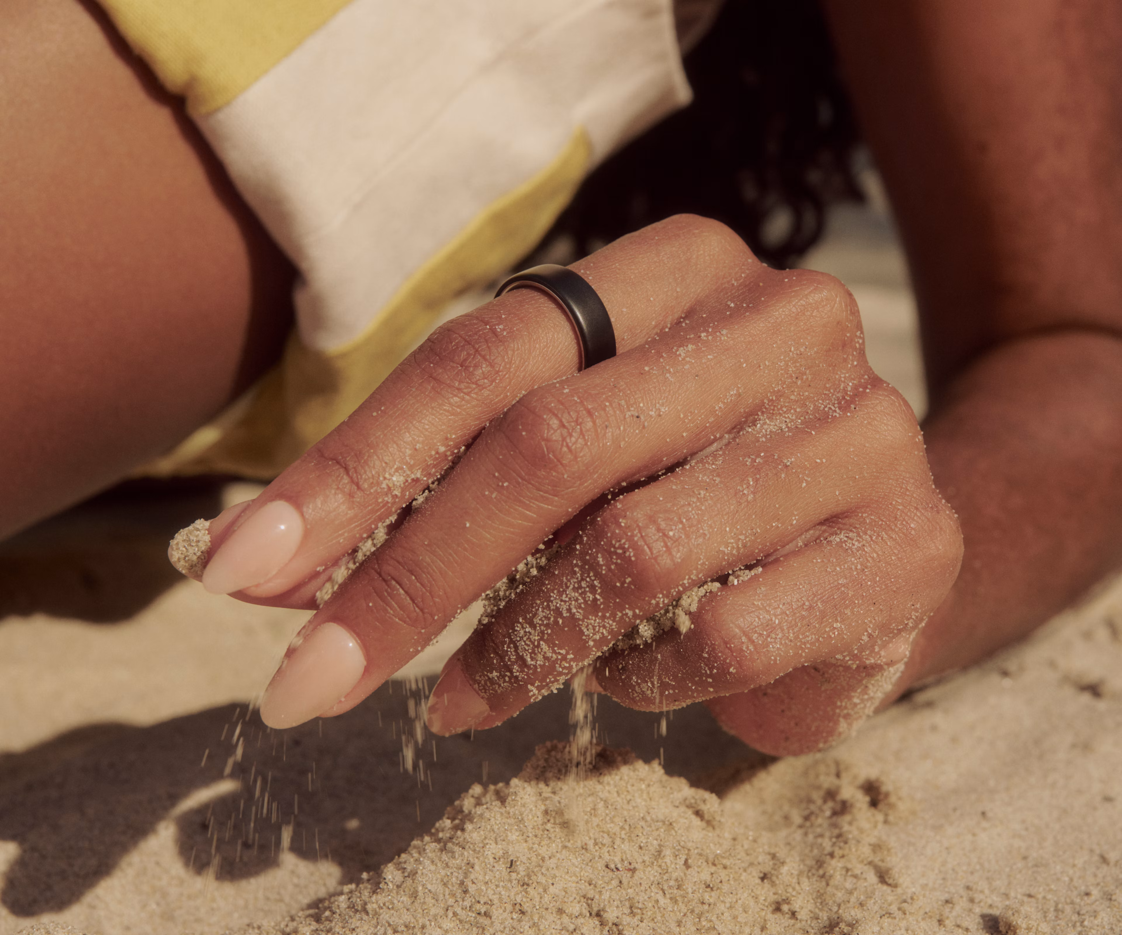 Close up of a person with their hand in the sand while wearing a Stealth Oura Ring 5.