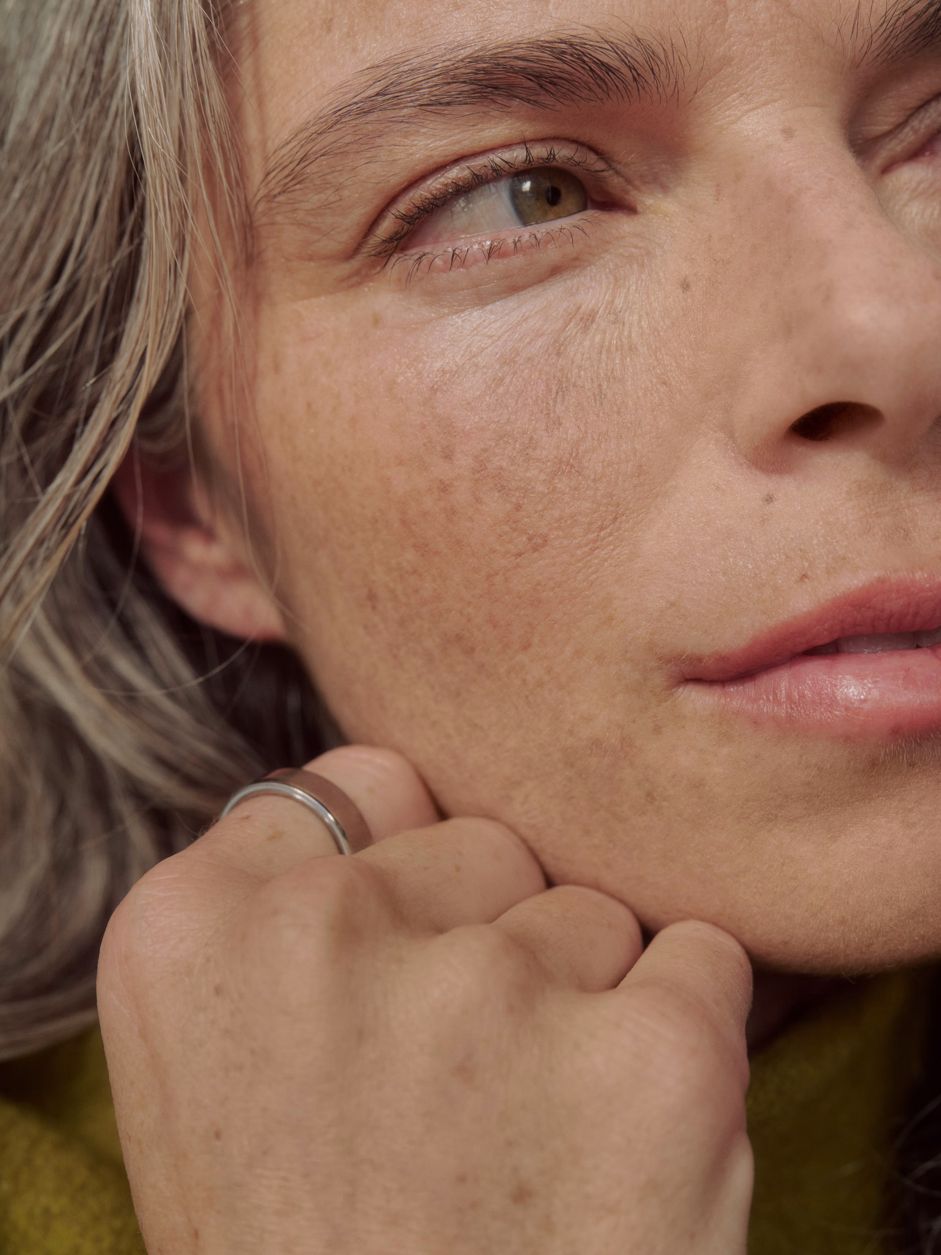 Woman with gray hair and freckles resting her chin on her hand, wearing a Silver Oura Ring.